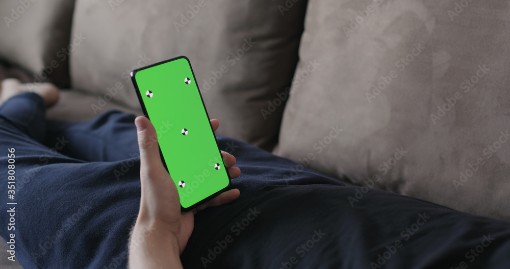 Closeup young man lying on a couch and holding smartphone with green screen Closeup young man lying on a couch and holding smartphone with green screen