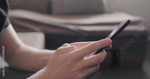 Closeup young man in black t-shirt typing messages on smartphone working from home side view
