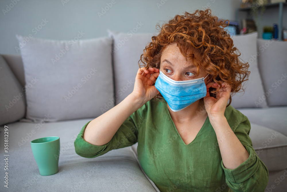 Portrait of young woman putting on a protective mask. Woman using mask. Sick red-haired woman using protective mask not to infect her family. Woman in Isolation Quarantine Coronavirus Portrait of young woman putting on a protective mask. Woman using mask. Sick red-haired woman using protective mask not to infect her family. Woman in Isolation Quarantine Coronavirus