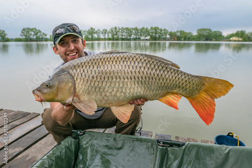 Carp fishing. Fisherman with fish trophy in hands at lake