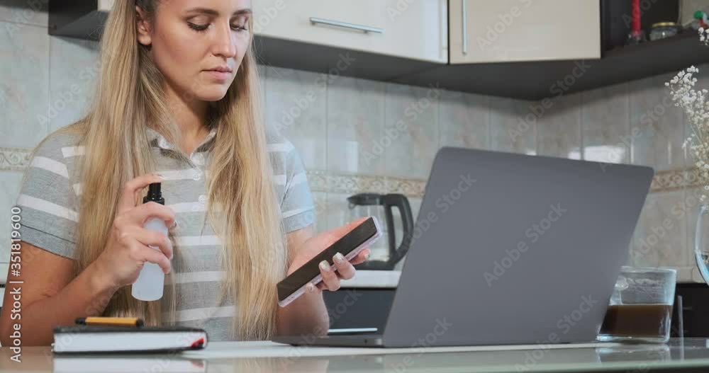 long haired girl blogger sprays antiseptic on black smartphone and wipes with paper napkin sitting at grey laptop slow motion long haired girl blogger sprays antiseptic on black smartphone and wipes with paper napkin sitting at grey laptop slow motion