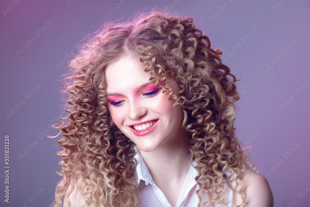 Portrait of a curly cheerful girl with professional make-up and retouching in the studio