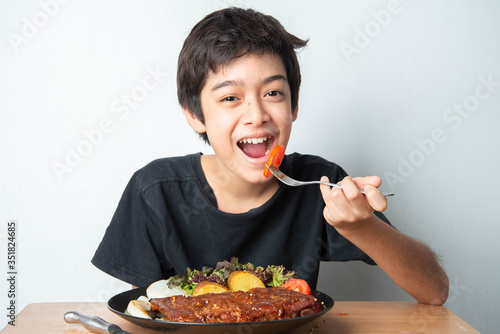 Little boy teenager eating tomato with salad for his meal