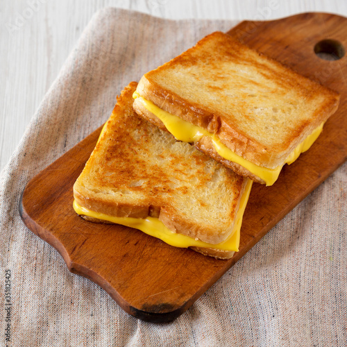 Homemade Grilled Cheese Sandwich on a rustic wooden board on a white wooden table, side view. Close-up.
