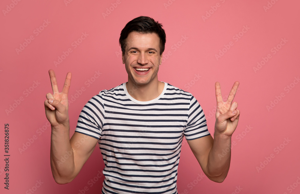 Peaceful man. Close-up photo of a happy man in a striped t-shirt, who is looking in the camera, smiling and showing two peace signs. Peaceful man. Close-up photo of a happy man in a striped t-shirt, who is looking in the camera, smiling and showing two peace signs.
