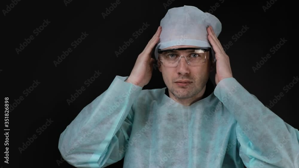 Portrait of a doctor surgeon who sits at a table and adjusts his hat and goggles on a black background. Portrait of a doctor surgeon who sits at a table and adjusts his hat and goggles on a black background.