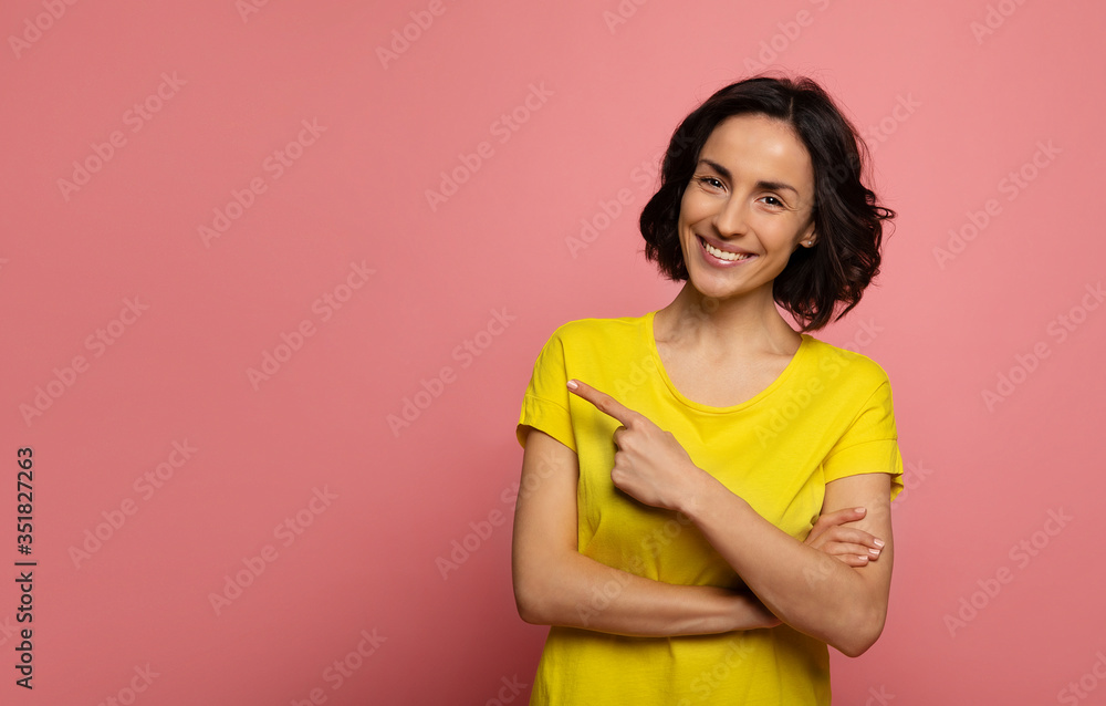 Pointing. Close-up photo of a happy woman in yellow t-shirt, who is looking in the camera and pointing to the left with her left index finger. Pointing. Close-up photo of a happy woman in yellow t-shirt, who is looking in the camera and pointing to the left with her left index finger.