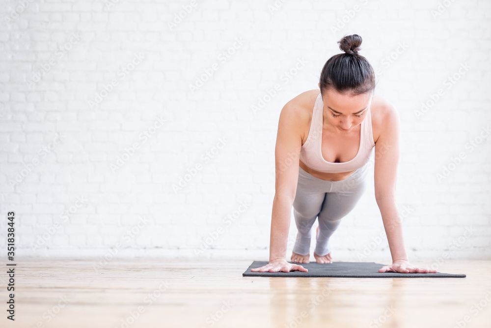 Pretty young woman doing push ups or press ups exercise phalankasana Plank pose on a rug in an empty gym. Concept of a strong body and beautiful figure. Advertising space