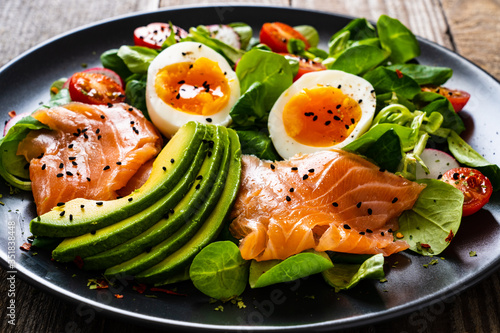 Salmon salad - smoked salmon boiled egg and vegetables on wooden background
