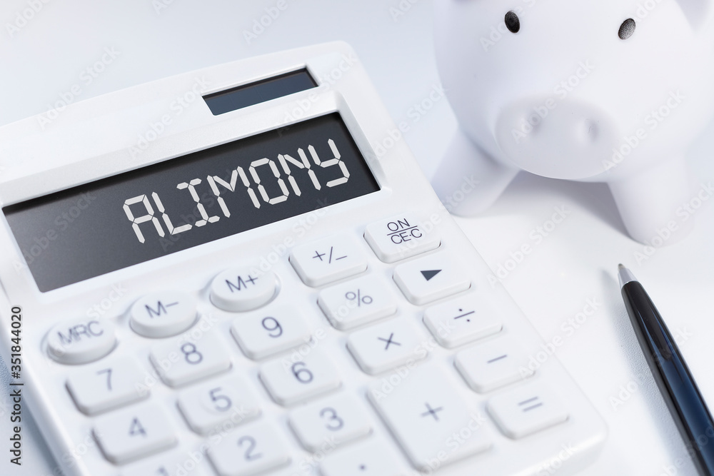 white calculator, white piggy and black pen with text ALIMONY on white background white calculator, white piggy and black pen with text ALIMONY on white background