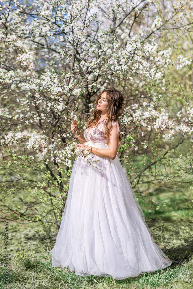 beautiful pregnant woman in a long light dress walks in a blooming spring garden in the spring garden