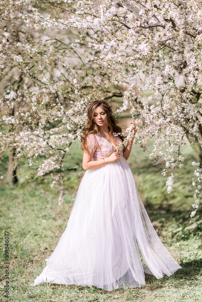 beautiful pregnant woman in a long light dress walks in a blooming spring garden.
