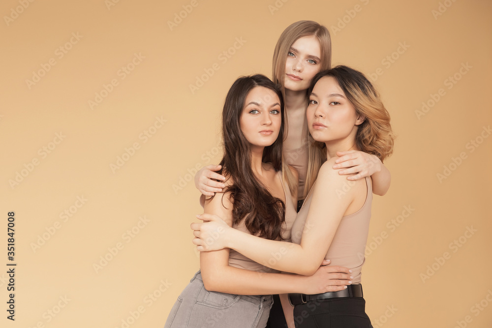 Happy young multicultural Asian women, Caucasian hugging and laughing in studio on beige background. Beauty spa treatment skin care concept