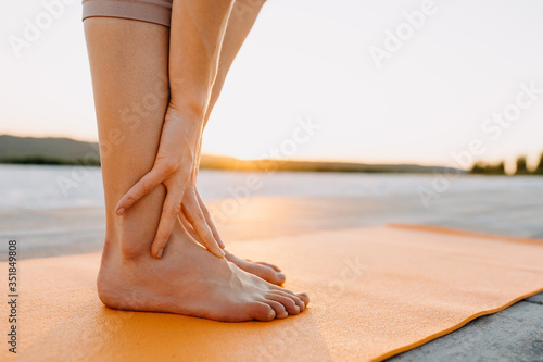 Young woman standing on a sport yoga mat, at the sunset, outdoors. Pilates teacher doing body stretching exercise. © Bostan Natalia