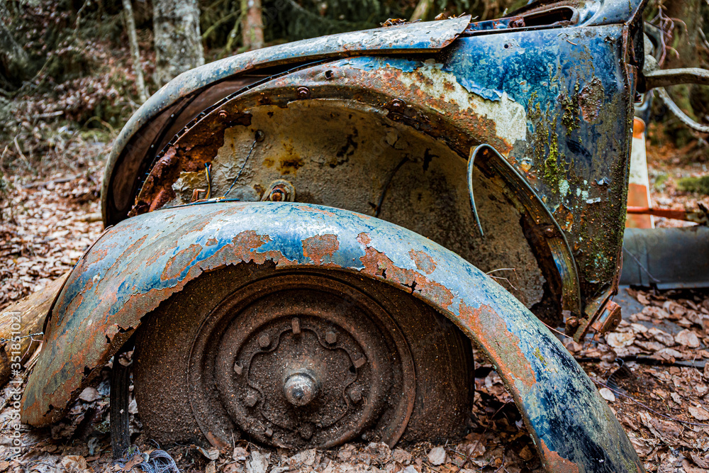 Bastnas, Sweden - APRIL 04, 2020: The wheel of a rusty Beetle with a loose wheel guard left behind in the mud at Ivan's Junk Yard - a deserted car cemetery far out in the Swedish woods