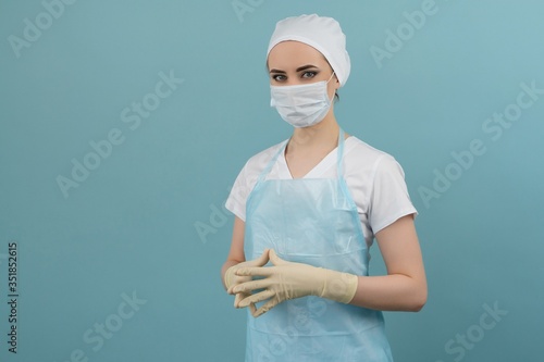 masked doctor in apron and gloves preparing for surgery on blue background