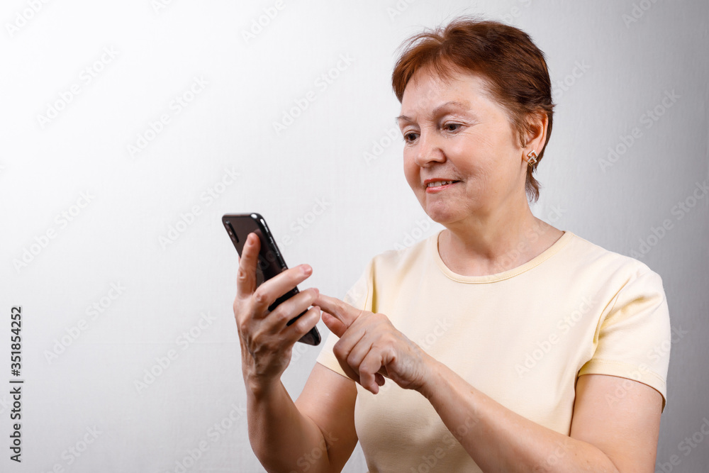 senior woman looks at the phone on a white background in a light T-shirt. place for text, isolated senior woman looks at the phone on a white background in a light T-shirt. place for text, isolated