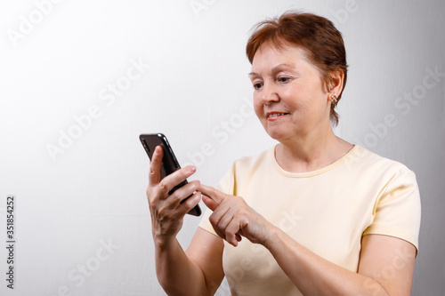 senior woman looks at the phone on a white background in a light T-shirt. place for text, isolated