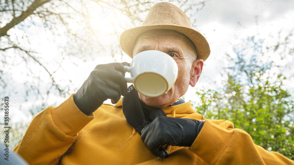 old man in yellow hoodie holds face mask and drinks tea old man in yellow hoodie holds face mask and drinks tea