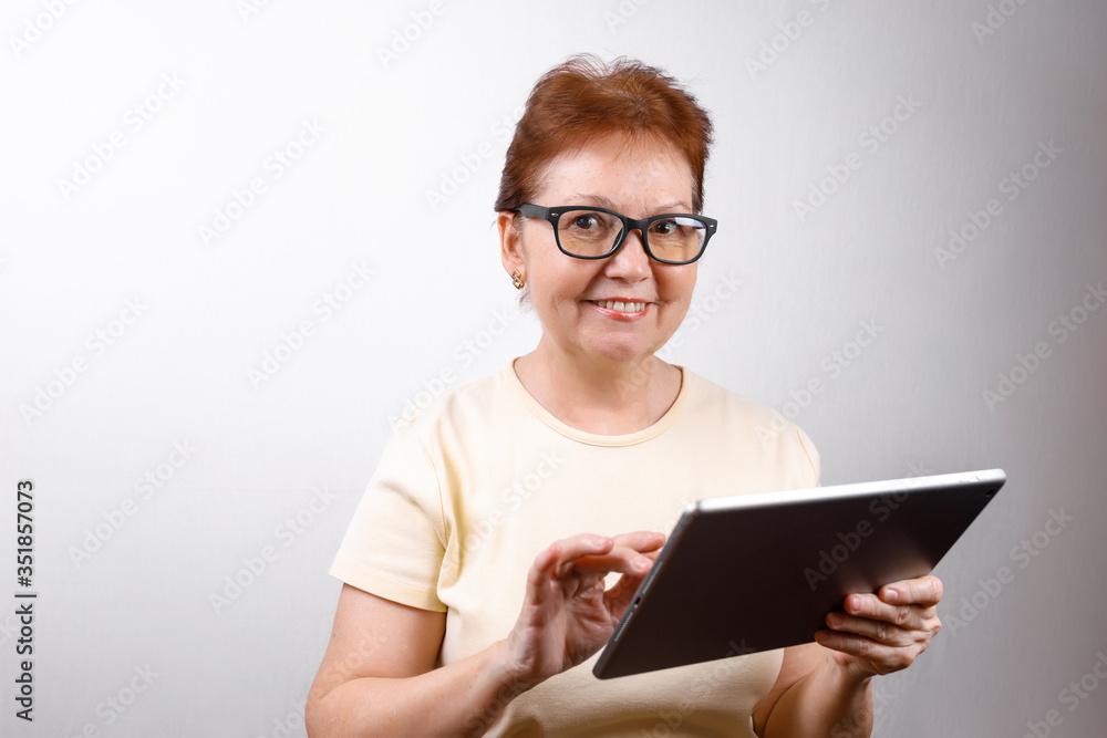 senior woman in glasses with a tablet on a white background in a light T-shirt. place for text, isolated senior woman in glasses with a tablet on a white background in a light T-shirt. place for text, isolated