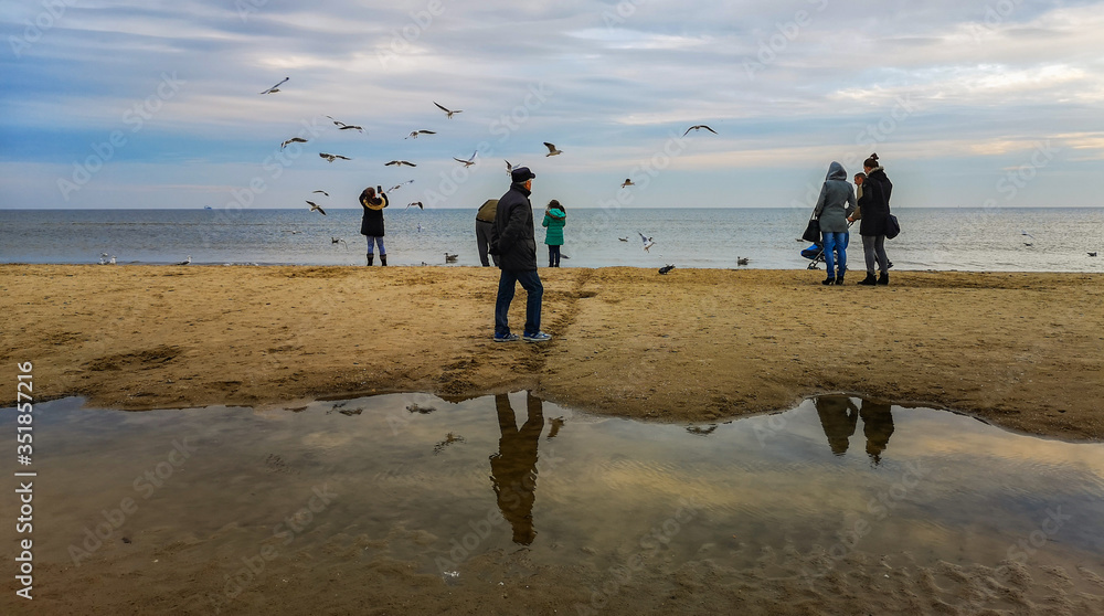 Beach near baltic sea in Swinoujscie in november with walking people flying seagulls and reflections in puddle