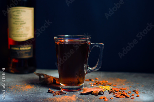 Grog with tea and rum, cinnamon and clove, rum bottle background.