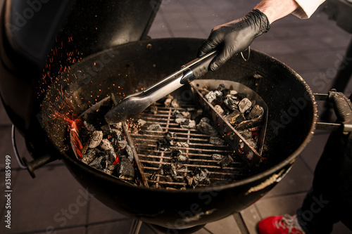 Close-up. Male cook in black gloves neatly transfers coals to the grill using tongs