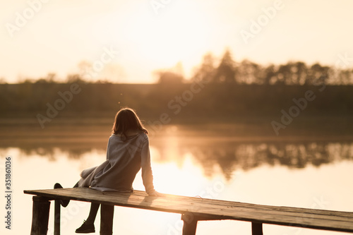 The girl spends time by the water in the woods. Dressed in a cardigan. Have fun and watch the sunset.