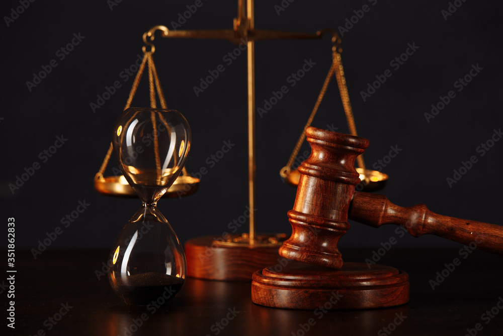 Law and justice concept. Lawyers desk. Judge's gavel, scales, hourglass, wooden table. Dark gray bokeh background Law and justice concept. Lawyers desk. Judge's gavel, scales, hourglass, wooden table. Dark gray bokeh background