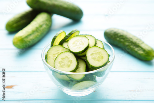 Fresh cucumber slices in bowl on blue wooden background.