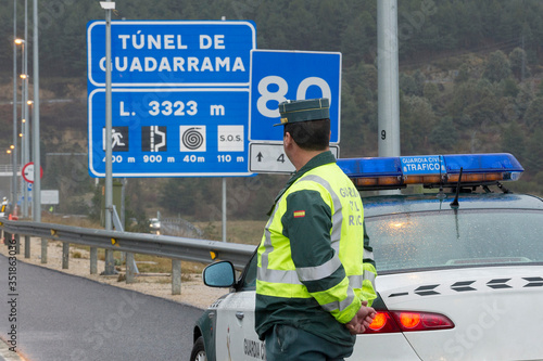 Guardia Civil next to his car watches traffic on a highway on a rainy day