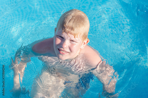 a disgruntled boy is sitting in the pool. a blond little hero gets angry at his parents while swimming in an outdoor pool. Child having fun in swimming pool.