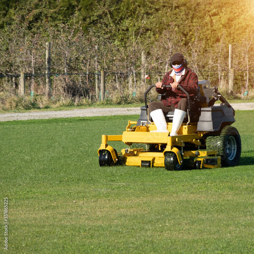 Soft focus of Gardener use Lawn mover on green grass in the modern garden, Machine for cutting lawns, the orange sunlight splashes behind and the green background fence, mow the lawn service concept. 
