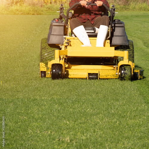 Soft focus of Gardener use Lawn mover on green grass in the modern garden, Machine for cutting lawns, the orange sunlight splashes behind and the green background fence, mow the lawn service concept.
