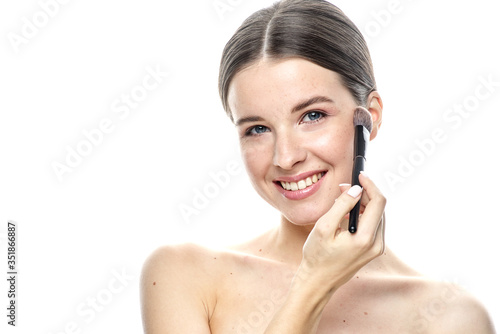 close-up portrait of a young brunette girl with blue eyes with clear skin, doing makeup with makeup brushes, isolated on a white background. High-resolution photos