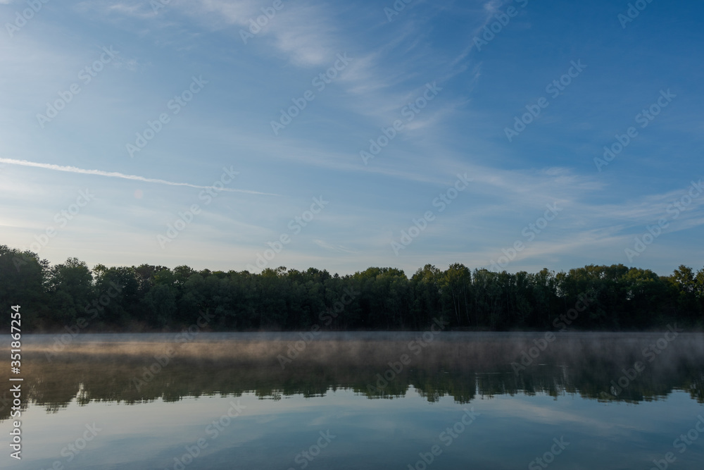 Small local recreation swimming lake in Bavaria, Germany in early morning light with fog over water