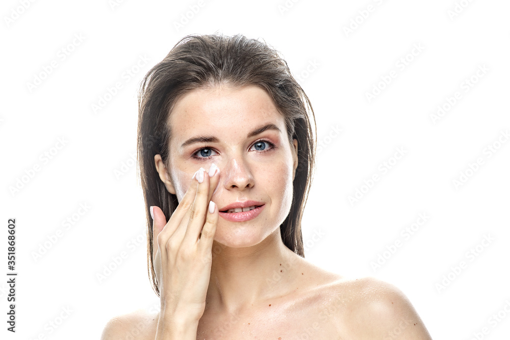 a close-up portrait of a young brunette girl with blue eyes with clear skin who applies cream to the face, isolated on a white background. High-resolution photos a close-up portrait of a young brunette girl with blue eyes with clear skin who applies cream to the face, isolated on a white background. High-resolution photos