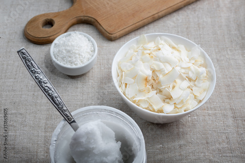 Bowl of coconut flakes and jar of coconut oil on fabric background. Superfoods.