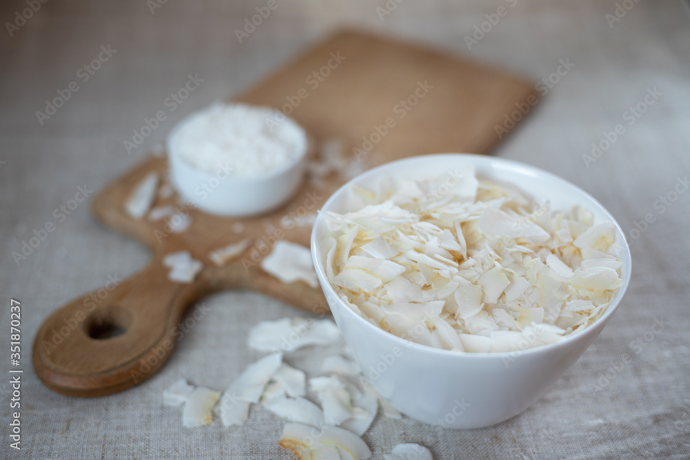 Coconut chips and shavings in a bowl on a cloth tablecloth and cutting board Coconut chips and shavings in a bowl on a cloth tablecloth and cutting board
