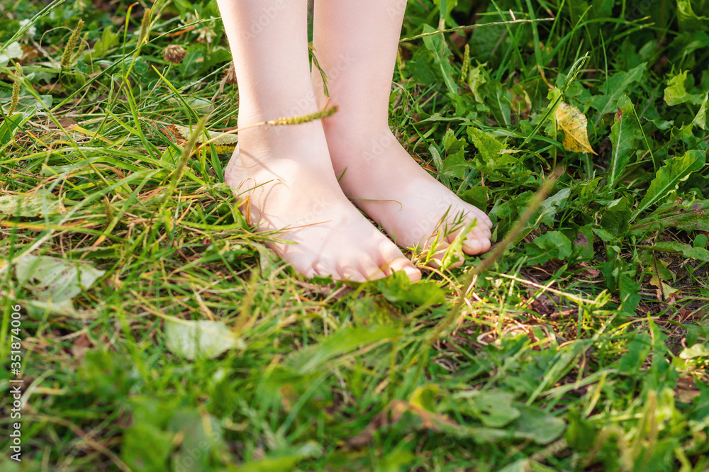 Feet of little kid standing on green grass outdoors. Barefoot on grass.