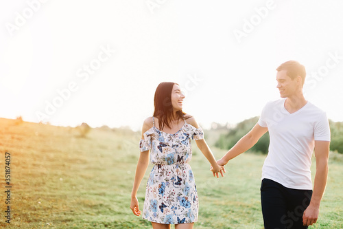 Young couple in love run on through grass field. Walking along grass field. © zadorozhna