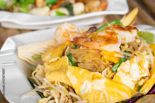 Omelet wraped Pad Thai with fresh shrimp in white dish on bamboo table, Fried white noodle.