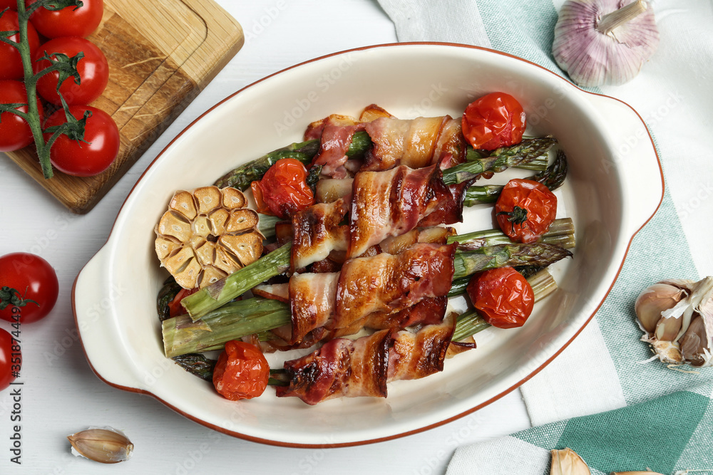 Oven baked asparagus wrapped with bacon in ceramic dish on white wooden table, flat lay Oven baked asparagus wrapped with bacon in ceramic dish on white wooden table, flat lay