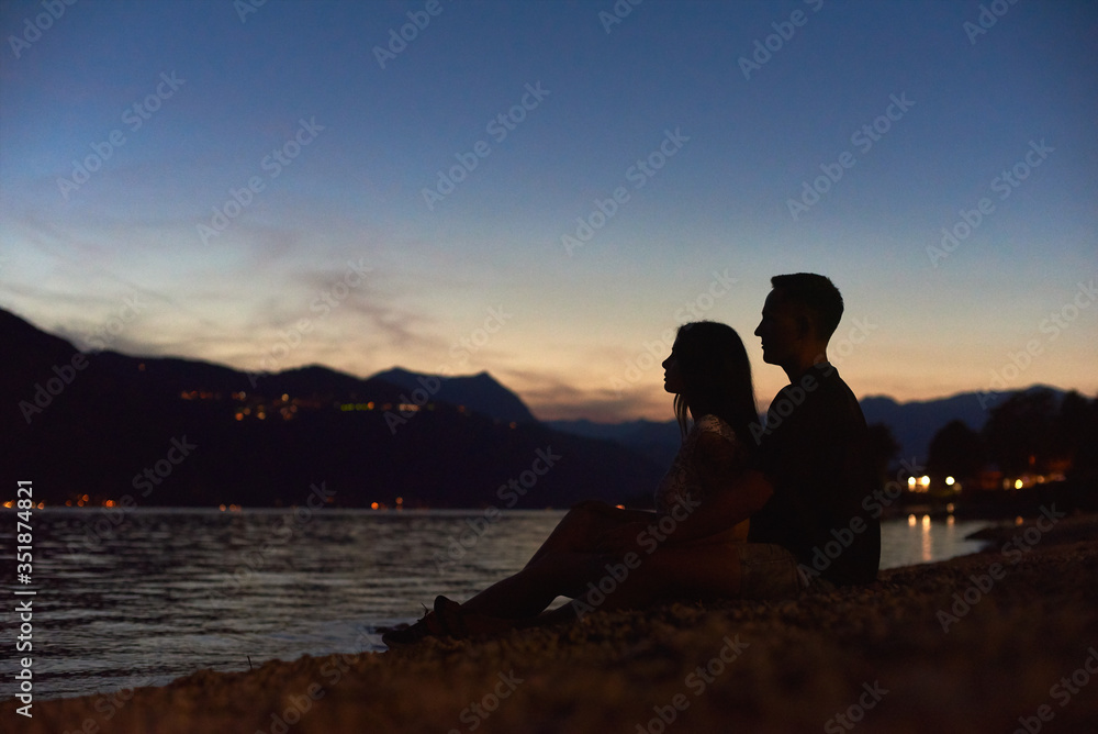 Side view silhouettes of happy young couple enjoying beautiful sunset on the beach. Boyfriend and girlfriend sharing tender moment by the sea. Concept of love, romance and relationships.