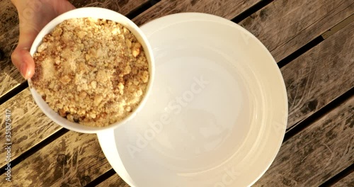 Putting a bowl of crushed nuts in a white plate
