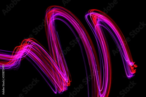 Long exposure photograph of neon colour in an abstract swirl  parallel lines pattern against a black background. Light painting photography.