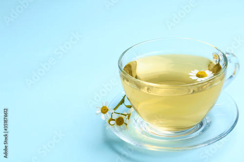 Delicious chamomile tea in glass cup on light blue background. Space for text