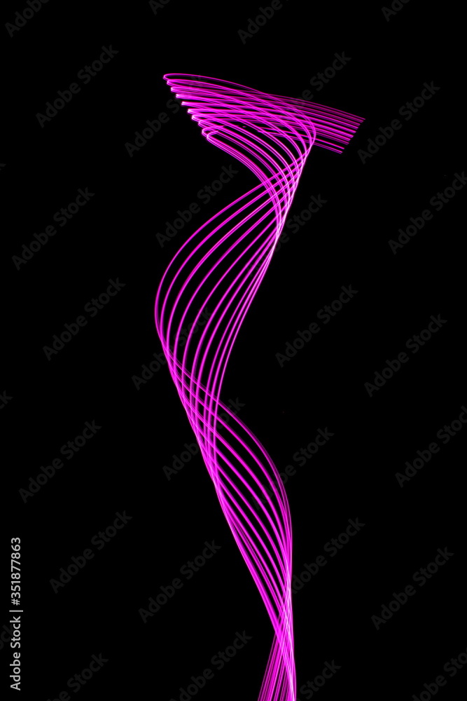 Obraz premium Long exposure photograph of neon pink colour in an abstract swirl, parallel lines pattern against a black background. Light painting photography.