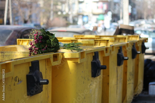 Bouquet of flowers is laying on the top of rubbish bin. © Nattasvi