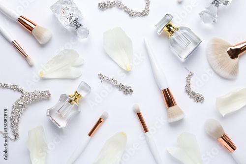 Bottles of perfume, makeup brushes and accessories on white background, flat lay